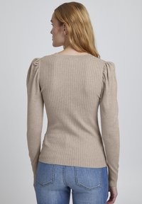 Beige ribbad tröja med puffiga axelsömmar, figursydd silhuett och långa ärmar, ihopparad med ljusblå denimjeans.