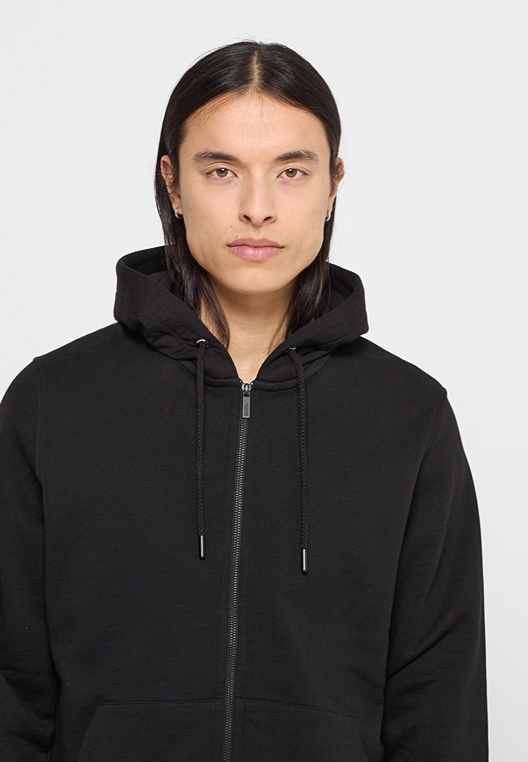 Czarna bluza z kapturem na zamek, z regulowanym kapturem, wykonana z miękkiego materiału. Posiada przednią kieszeń oraz prosty, minimalistyczny design.