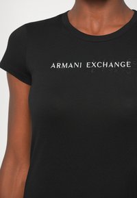 Camiseta de algodón negra de manga corta con el texto "Armani Exchange" en blanco, colocado en el centro y parcialmente en relieve.