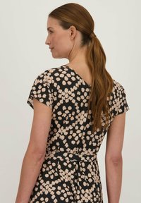 Zwarte jurk met lichtbeige polkadotpatroon, korte mouwen, V-hals aan de achterkant en een aansluitende taille. Soepele stof met lichte glans.