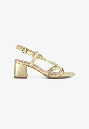 Sandal de talón bajo en dorado con diseño de tiras entrecruzadas con acentos metálicos y un material superior liso y brillante.