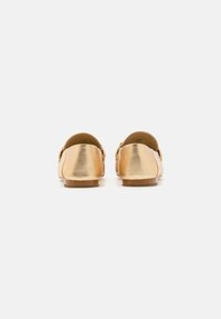 Auksinės metalinės slip-on bateliai su tekstūruotu paviršiumi, žemu kulnu ir apvaliu užpakaliu. Minimalistinis dizainas be matomų tvirtinimo elementų.