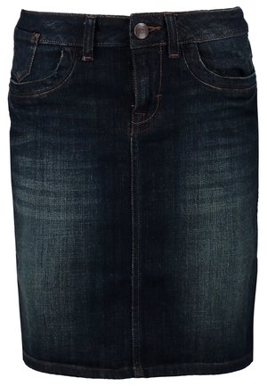 Vrouw draagt zwarte blouse, donker denim rokje, doorschijnende zwarte panty's, zwarte enkellaarsjes, draagt zwarte leren handtas, geaccentueerd met zilveren armbanden.