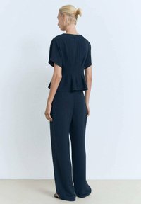 Tmavě modrý dvoudílný outfit složený z volného topu s krátkými rukávy a peplum, doplněný širokými kalhotami. Texturovaná tkanina.