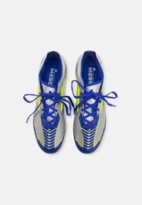 Scarpe da calcio blu e grigie con un design testurizzato, caratterizzate da brillanti accenti gialli e lacci blu, viste dall'alto.
