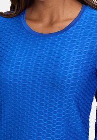 Niebieska, teksturowana koszula z długim rękawem i okrągłym dekoltem, ozdobiona subtelnym wzorem wypukłych heksagonów, wykonana z rozciągliwego materiału.