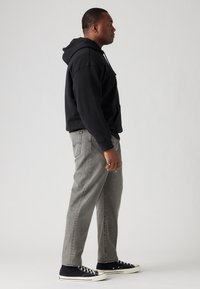 Sudadera negra con bolsillo canguro, jeans grises de pierna recta y zapatillas negras con suelas blancas. Diseño sencillo, sin patrones o acentos visibles.