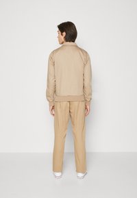 Chándal beige que presenta una chaqueta con cremallera y cuello, con puños elásticos, combinada con pantalones holgados. Tejido suave, detalles mínimos.