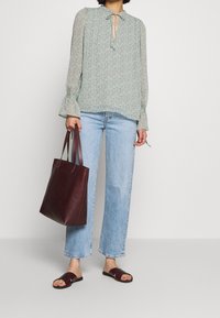 Ljusgrön blommig blus med knytkrage, vida ärmar, tillsammans med ljusblå raka jeans och en vinröd läderhandväska.