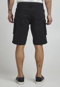 Black cargo shorts made of denim, featuring two back pockets and side pockets. Beneath the knee length, with a straight cut and subtle texture.