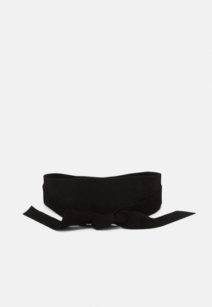 Ceinture large en tissu noir nouée en nœud avec de longues extrémités sur un fond blanc uni.