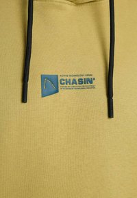 Rumena jopa s črnimi vrvicami, na prsih modra znamka in napis "CHASIN' Active Technology Denim".