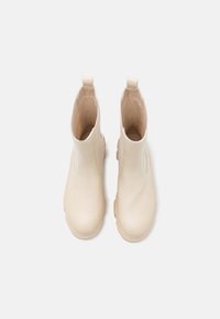 Une paire de bottines en cuir beige avec des tirants et des semelles épaisses, vues de dessus sur un fond blanc.