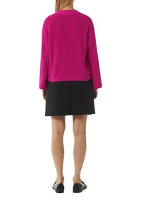 Fuchsia gestrickter Pullover mit langen Ärmeln, strukturiertem Stoff. Kombiniert mit einem schwarzen Rock mit geometrischem Muster, abgerundet mit schwarzen Schuhen.