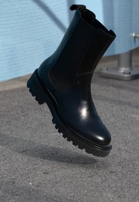 Black leather Chelsea boot with elastic sides and a rugged rubber sole, featuring a polished finish and a rounded toe design.