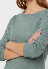 Maglione lavorato a maglia di un verde tenue e morbido con un motivo testurizzato, colletto rotondo aderente e maniche leggermente arricciate.