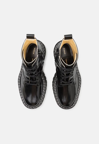 Schwarze Leder-Ankle-Boots mit glänzender Oberfläche, runder Zehenpartie und weißen Nähdetails entlang der Sohle. Enthält Schnürung und Zuglaschen-Details.