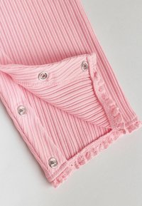 Tissu rose côtelé avec boutons-pression argentés et bordure en dentelle festonnée, partiellement dénoué sur une surface claire.