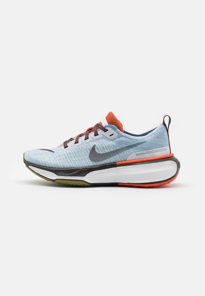Světle modré běžecké boty s texturou síťoviny, oranžovými akcenty, černobílou podrážkou a hnědými tkaničkami. Logo Nike na straně.