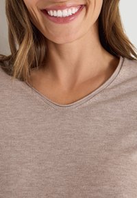 Beige Oberteil mit rundem Ausschnitt, aus einem weichen, strukturierten Stoff. Nahaufnahme, die die glatte Oberfläche und subtile Nähdetails zeigt.