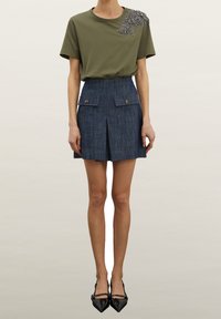 T-shirt en coton vert olive avec des détails perlés sur l'épaule, associé à une jupe en jean foncé avec pli à l'avant et poches plaquées.