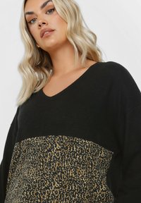 Mustapaita, jossa on leopardikuvioinen paneeli alaosassa. Kangas näyttää pehmeältä, ja siinä on rento istuvuus sekä pitkät hihat.