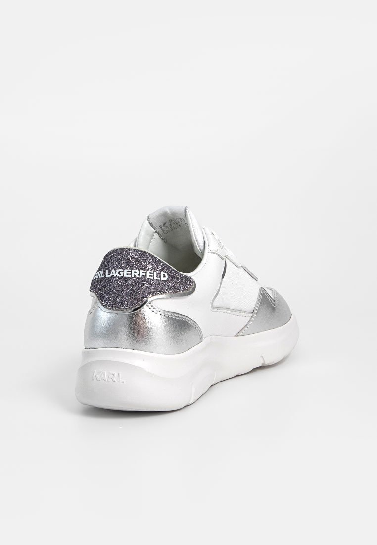 Sneaker blanc et argent avec un talon noir pailleté étiqueté "KARL LAGERFELD," vu de l'arrière et incliné vers la gauche.