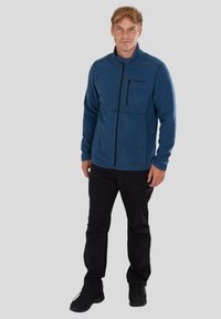 Blue fleece jacket with a high collar, front zipper, and a chest pocket. Black pants and black shoes complete the outfit.