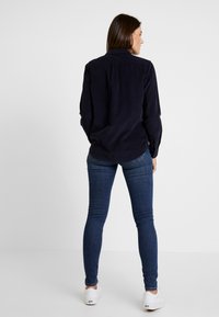 Mörkblå kordfløjelskjorta med långa ärmar, krage och knappdetaljer, i kombination med åtsittande mörkblå jeans och vita sneakers.