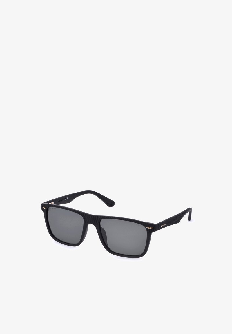 Lunettes de soleil rectangulaires noires avec des verres foncés et des détails subtils d'ailes dorées sur les branches, légèrement inclinées vers la droite sur fond blanc.