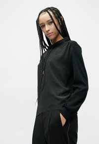 Czarny pulower z kapturem, długimi rękawami, lekką fakturą, z subtelnymi przeszyciami i luźnym krojem. Połączony z ciemnymi spodniami.