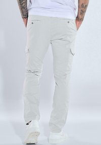 Helle graue Cargo-Hosen mit slim fit, die seitliche Taschen, eine glatte Textur und dezente Nähtdetails aufweisen. Tragen mit weißen Sneakers.