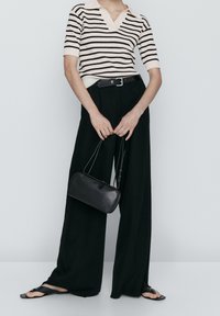 Top en maille rayé crème et noir, pantalon large noir, sac à main en cuir noir, et sandales plates. Textures clés et couleurs contrastées.