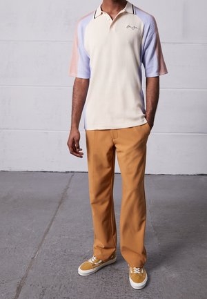 Polohemd in crème, lichtblauw en lichtroze met een geribbelde textuur; gecombineerd met beige broek; afgewerkt met gele sneakers en witte zolen.