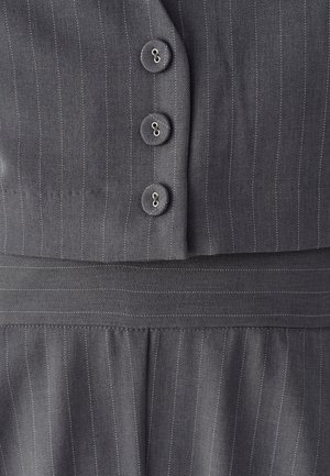 Tissu à fines rayures grises avec trois boutons assortis alignés verticalement sur un vêtement sur mesure, montrant les détails de couture et de la ceinture.