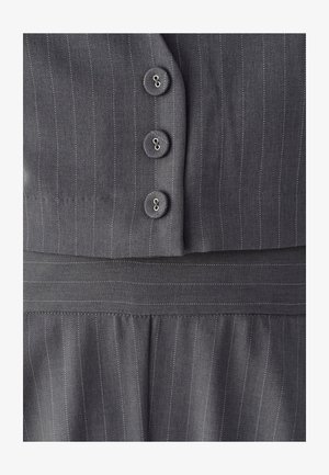 Tissu à fines rayures grises avec trois boutons assortis alignés verticalement sur un vêtement sur mesure, montrant les détails de couture et de la ceinture.