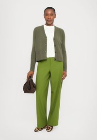 Olive green ribbed cardigan with black buttons, white crew-neck shirt, green wide-leg trousers, and brown bag. Shoes feature a leopard print.