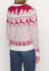 Stickad tröja med vit bas och röda och rosa julmotiv, inklusive renar, träd och snöflingor, med ribbade ärmslut och nederkant.