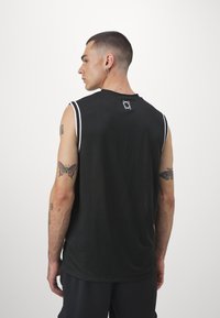 Μαύρη αθλητική μπλούζα χωρίς μανίκια με λευκές λεπτομέρειες, στρογγυλή λαιμόκοψη και λογότυπο στην πλάτη. Το ύφασμα φαίνεται ελαφρύ με λεία υφή.