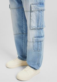 Ljusblå denim cargobyxor med flera fickor och en avslappnad passform, kombinerade med vita sneakers med perforerade detaljer.