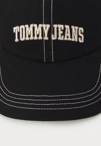 Black cap made of cotton with white stitching and embroidered "TOMMY JEANS" in gold thread on the front. Curved visor design.