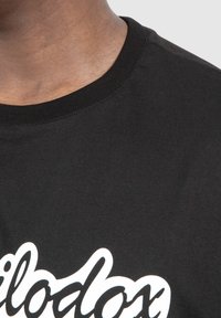 Camiseta de algodón negra con cuello redondo y diseño de texto gráfico blanco. Textura suave, con mangas cortas y un ajuste relajado.