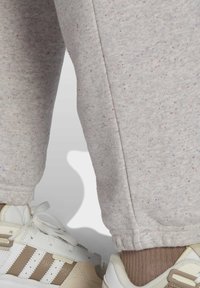 Underben klädda i ljusgråa, prickiga träningsoverallbyxor med elastiska muddar, kombinerade med beigea och vita sneakers samt ljusbruna strumpor.