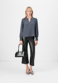 Langermet grå bluse med v-hals og rynkede mansjetter; kombinert med svarte bukser i imitert skinn i cropped stil og en liten svart håndveske. Nøytrale hæler.