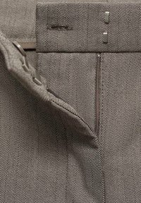 Material cu model houndstooth în nuanțe de bej și gri, cu o textură netedă. Dispune de un închidere cu fermoar și două accente metalice pe talie.
