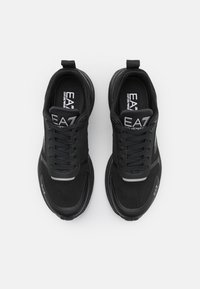 Zapatillas deportivas negras con una parte superior de malla texturizada, puntera redonda, diseño de cordones y acentos laterales; logo de la marca en la lengua y el lado.