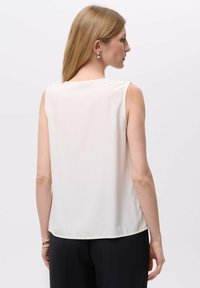 Bezramenný krémový top vyrobený z lehkého materiálu. Má zaoblený výstřih a rovný lem, což doplňuje minimalistický design.