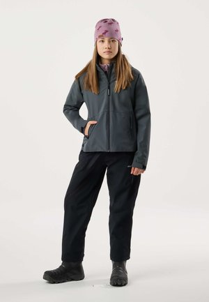 Young person standing wearing a pink beanie with moose prints, gray zip-up jacket, black pants, and black boots on white background.