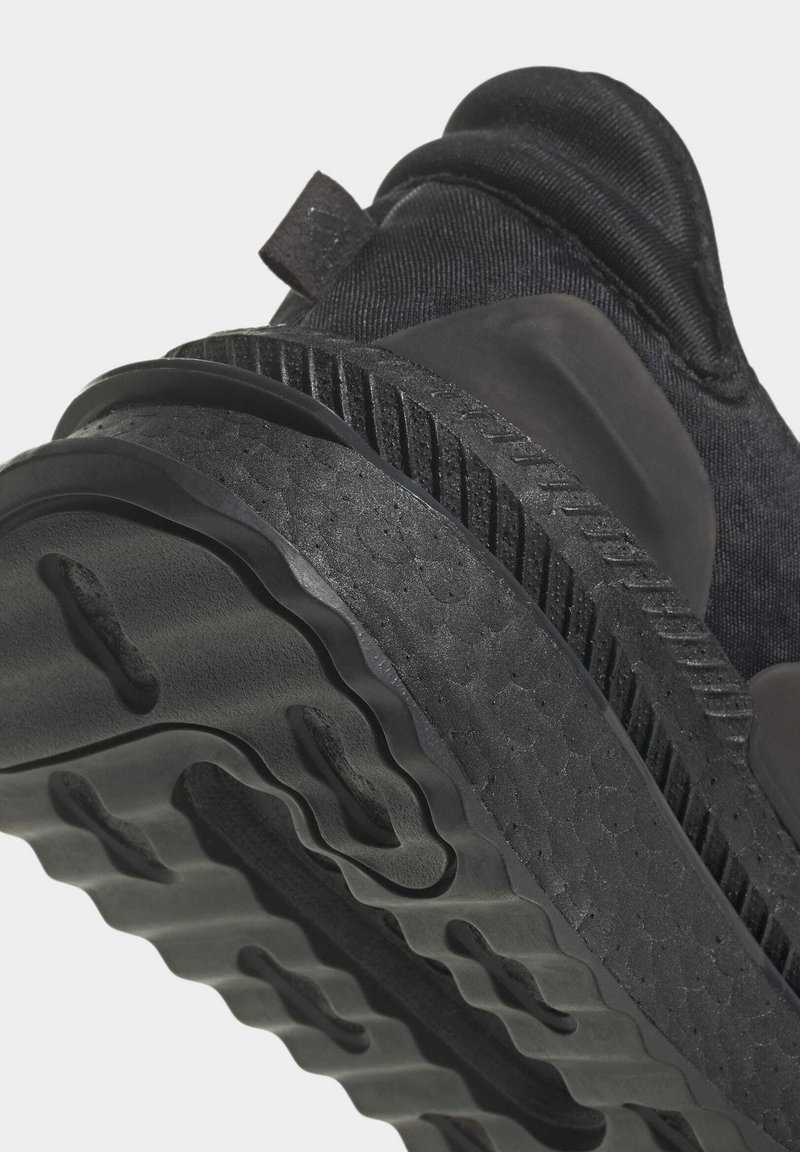 Schwarze Sport-Schuhsohle mit strukturiertem Gummi, wellenförmigem Muster und geschichtetem Dämpfungsdesign. Das Obermaterial zeigt eine glatte Stoffoberfläche.