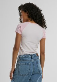 Fitted, short-sleeve t-shirt in soft pink and white cotton blend. Features raglan sleeves and a smooth texture. Paired with high-waisted blue jeans.